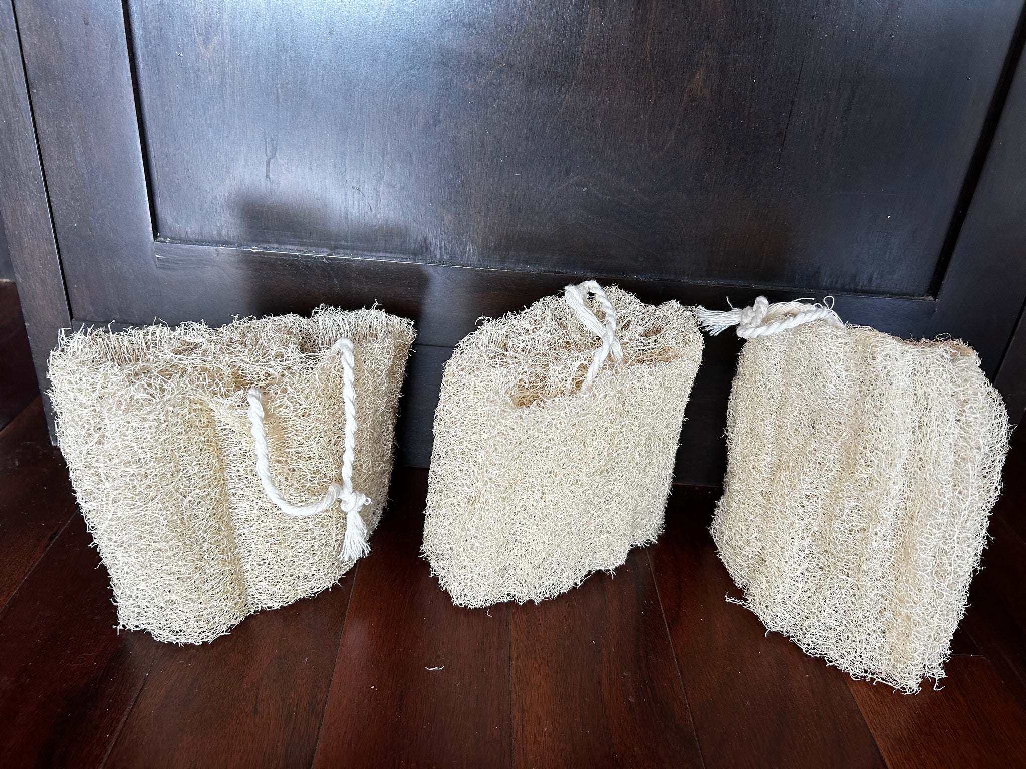 Three natural fiber sponges hanging against a dark wooden cabinet.